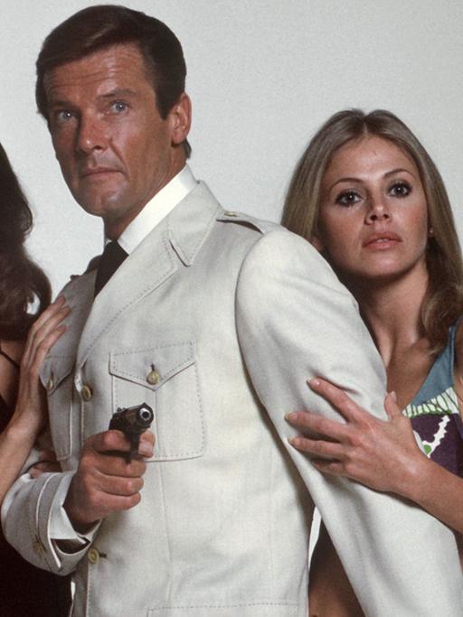 James Bond-Darsteller Roger Moore mit seinen Filmpartnerinnen Maud Adams (l.) und Britt Eklund (r.) in dem Film "Der Mann mit dem goldenen Colt"