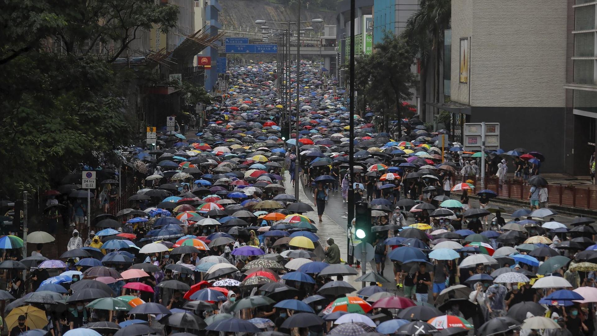 Ein langer Demonstrationszug mit tausenden Regenschirmen zieht eine breite Straße entlang durch eine Häuserschlucht.