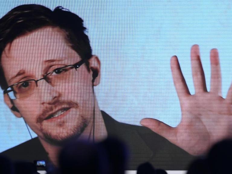 Über verschatteten Sitzreihen scheint ein auf die Bühne projizierter Stream auf, über den Edward Snowden an einer Konferenz teilnimmt.