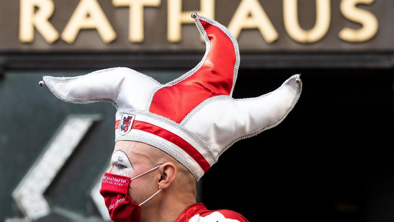 Ein Karnevalist mit Narrenkappe steht vor dem Rathaus in Düsseldorf