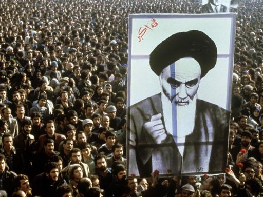 Iranische Bürger protestieren im Jahr 1979 gegen den Schah. Im Vordergrund ist ein riesiges Banner mit dem Abbild von Revolutionsführer Ruhollah Khomeini