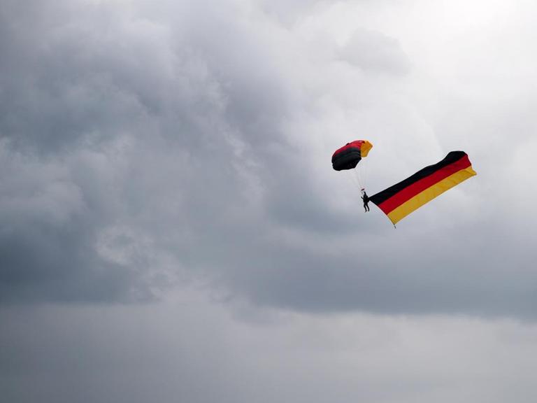 Ein Fallschirmspringer zieht eine Deutschlandfahne über dem Bürgerfest in Dresden hinter sich her.