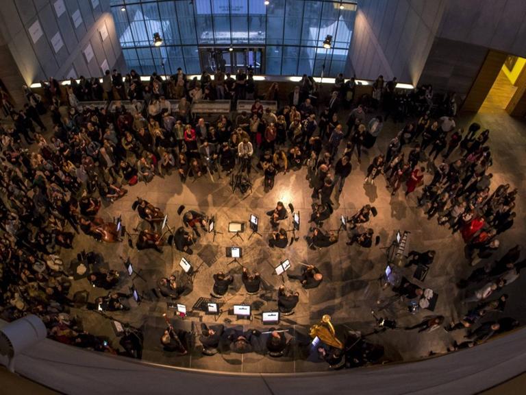 Eröffnung der Ausstellung "Peace Is Power" von Yoko Ono im Museum der bildenden Künste Leipzig. Die Kamera blickt von oben auf das Publikum und ein Orchester während der Eröffnungsveranstaltung, 2019.