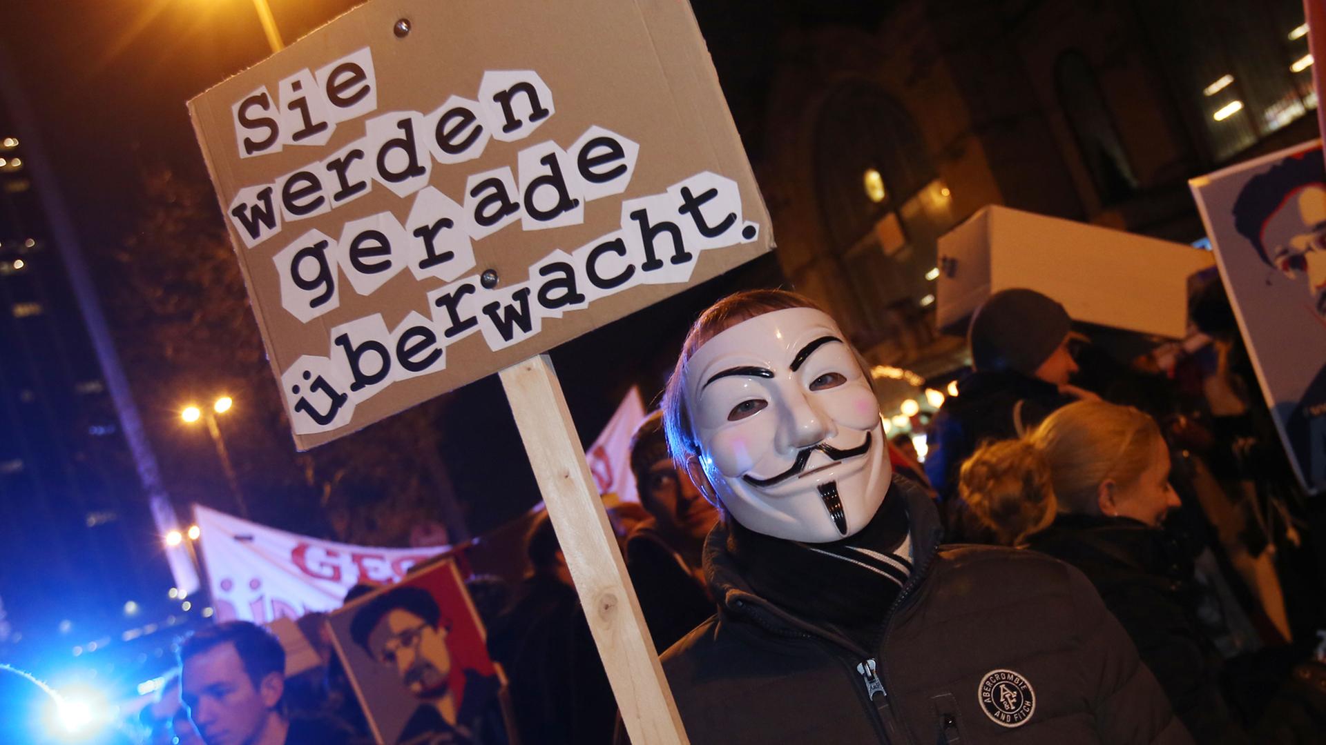 Teilnehmer des 31. Chaos Communication Congress demonstrieren am Congress Center in Hamburg mit dem Plakat "Sie werden gerade überwacht".