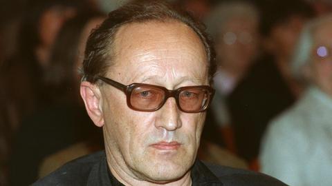 Heiner Müller trägt eine Brille mit rot-getönten Gläsern, er schaut missmutig in die Kamera