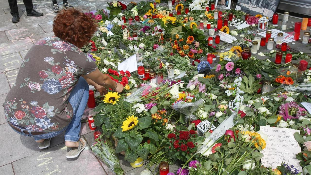 Eine Frau legt in Hamburg-Barmbek vor dem Supermarkt, in dem ein Mann einen Menschen mit einem Messer getötet hat, Blumen nieder. 