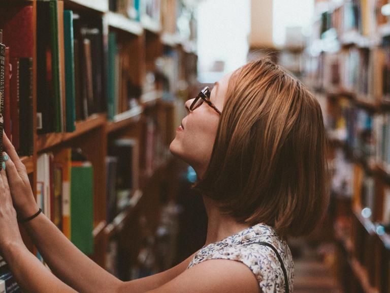 Eine Frau steht vor einem Regal voller Bücher.