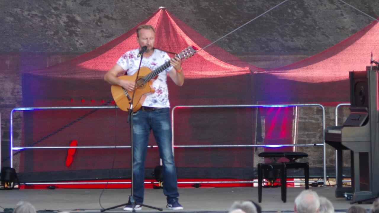Der Comedian und Musiker Helmut Sanftenschneider mit Gitarre auf der Bühne.