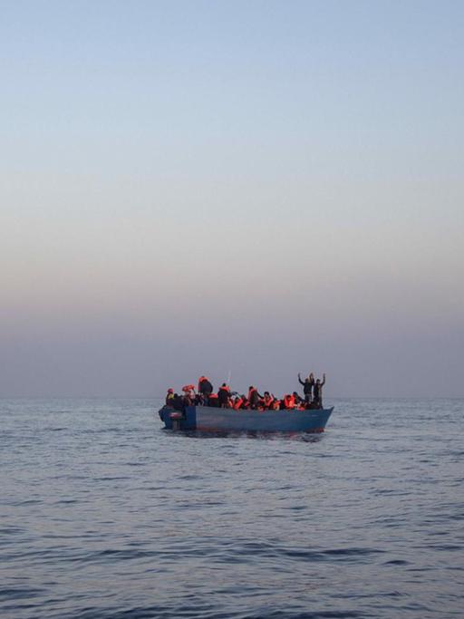 Bootsflüchtlinge aus Afrika und Asien winken auf einem Holzboot im Mittelmeer, 14 Meilen nördlich von Sabratha, Libyen, während sie auf ihre Rettung durch eine NGO warten