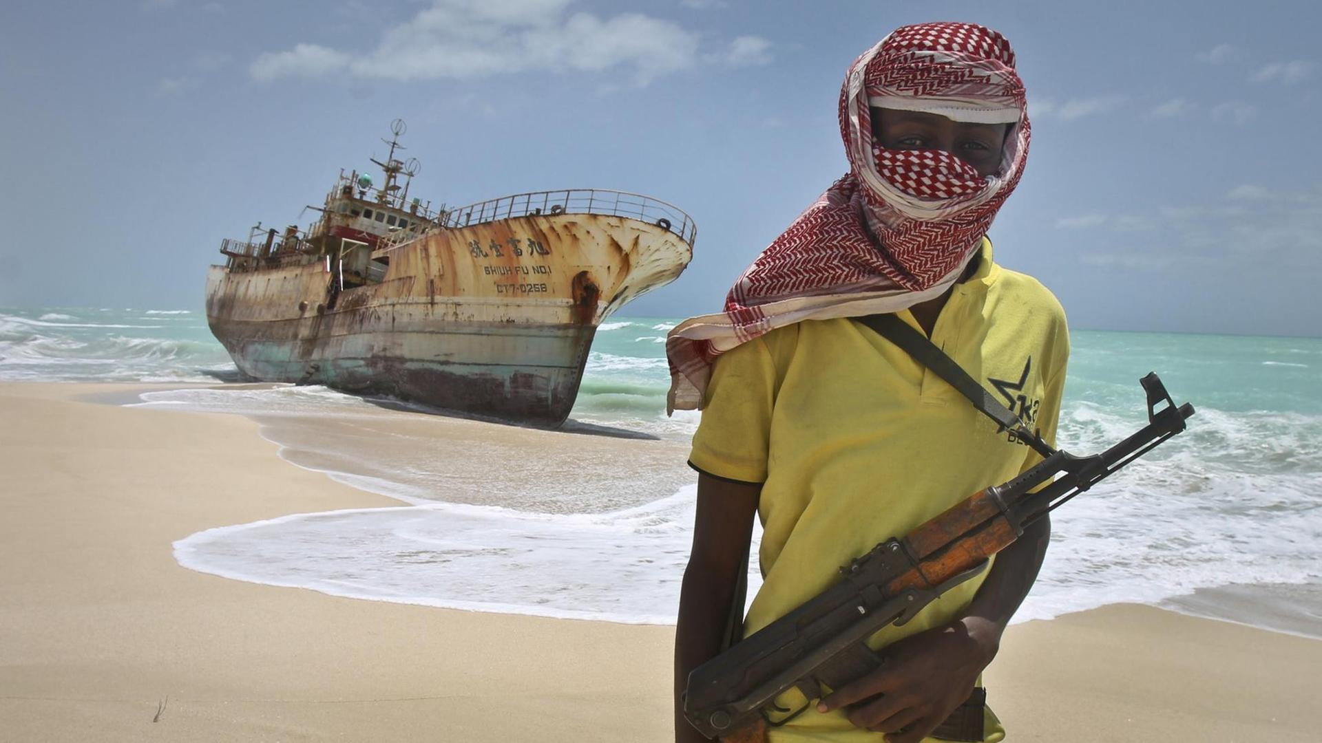 Ein somalischer Pirat steht am Strand vor einem Schiffswrack