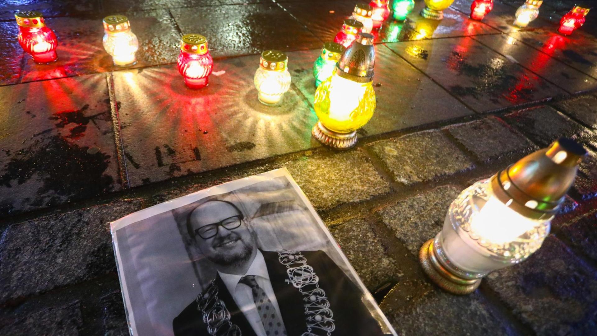 Auf einem Platz liegt im Dunkeln ein schwarz-weißes Foto von Adamowicz, daneben brennen  Gedenkkerzen.