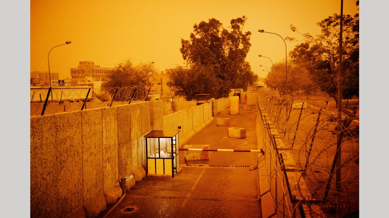 Der mit Betonwänden und Stacheldraht gesicherte Eingang zum Sitz der New York Times in Bagdad während eines Sandsturms 2006: Foto aus dem Bildband "hello camel" von Christoph Bangert über die Absurdität von Krieg
