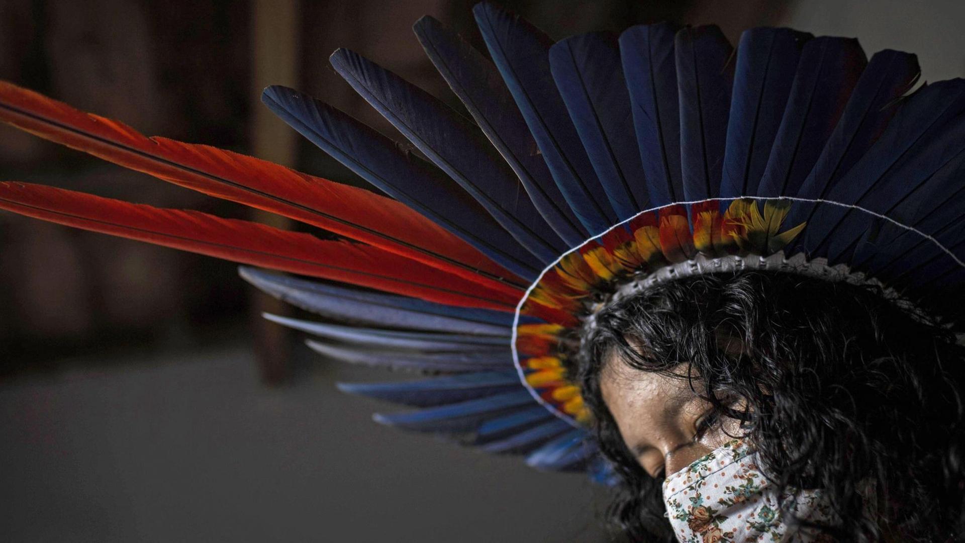 Eine Indigena in Brasilien mit einem Mundschutz und mit dem Kopfschmuck des Sateré-Mawé Volkes