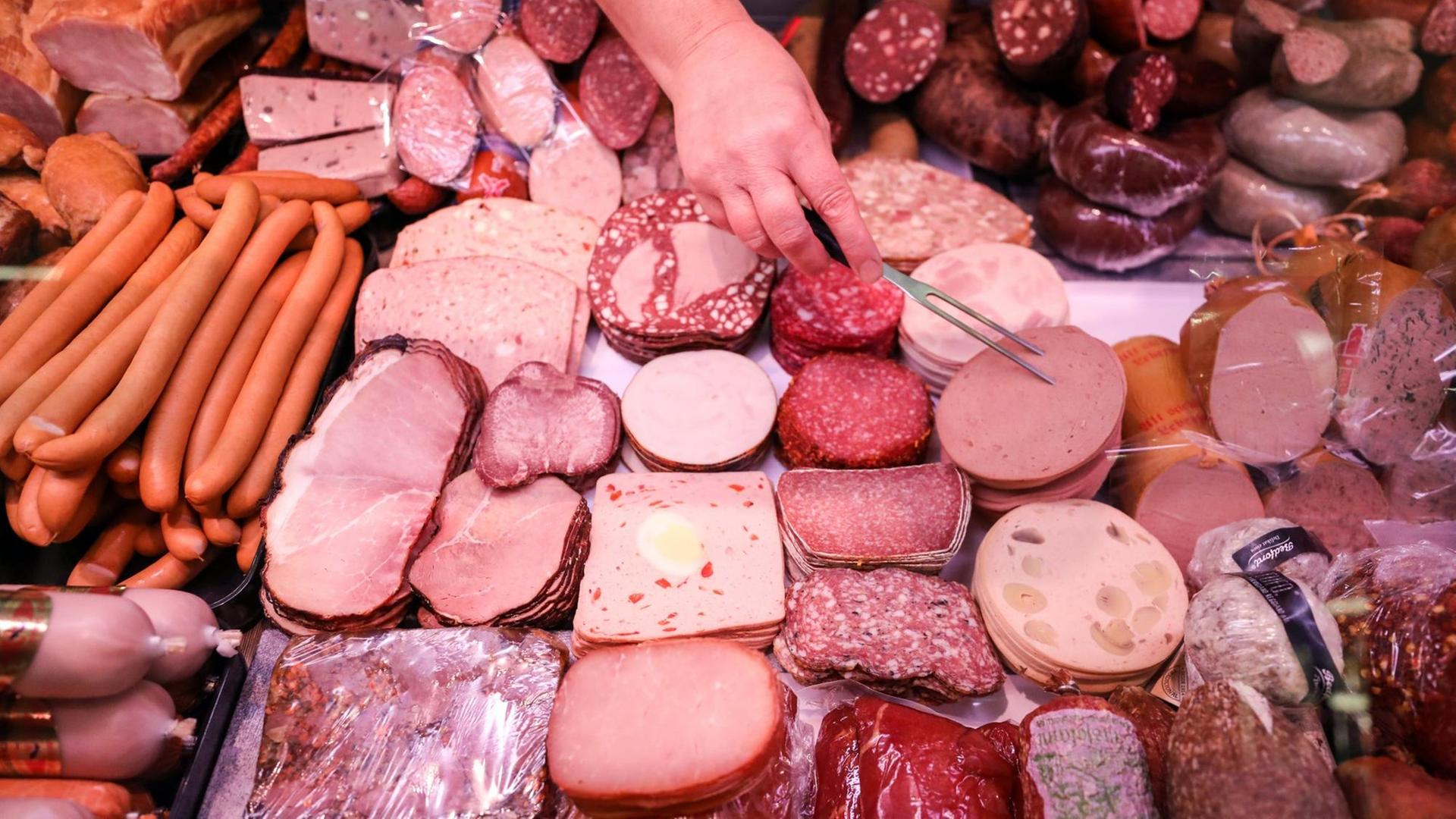 Eine Verkäuferin nimmt Leberkäse aus einer Fleischtheke in einem Supermarkt.