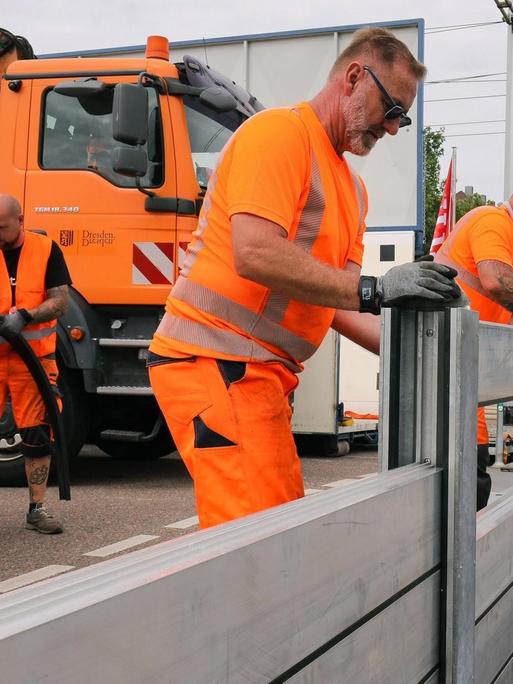 Mitarbeiter der Stadt Dresden bauen an einer Straße eine mobile Hochwasserschutzanlage zur Probe auf.