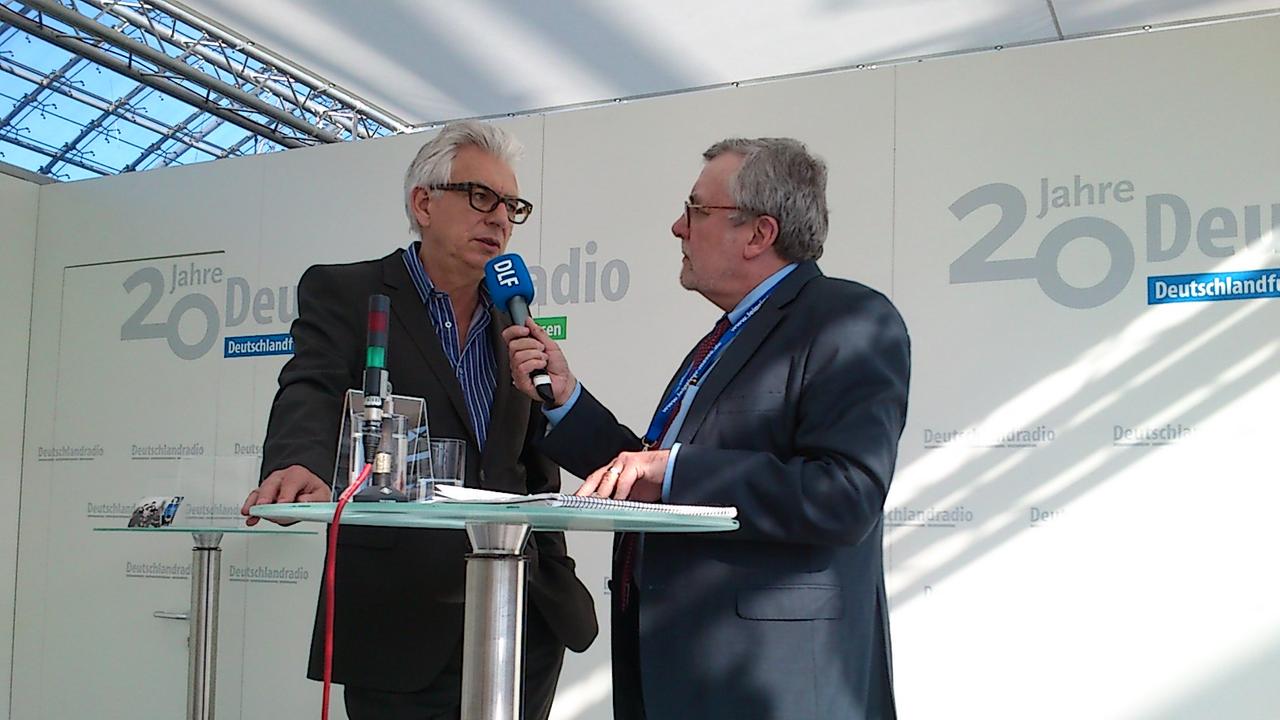 Der "Andruck"-Redakteur Thilo Kößler spricht am Messestand von Deutschlandradio mit dem Buchautor Stephan Wackwitz, beide sind im Halbprofil zu sehen.