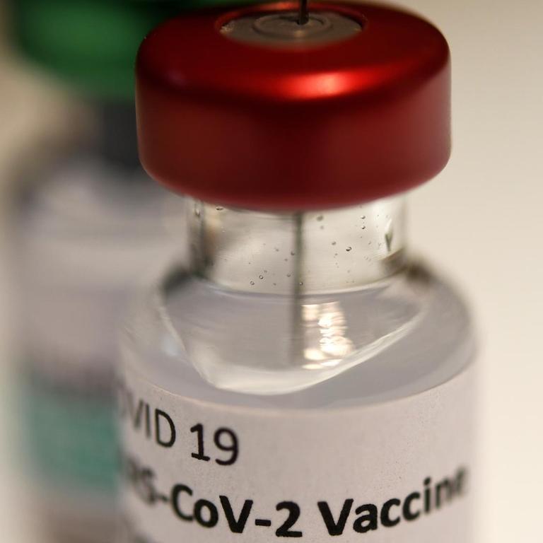 Eine Spritze steckt in einem Fläschchen mit dem Aufdruck "COVID-19 Vaccine"