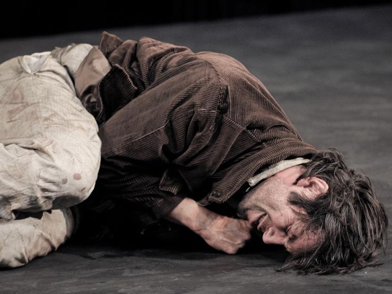 Bühnenszene, in der ein Mann (Max Simonischek als Georg) zusammengekauert auf dem Boden liegt