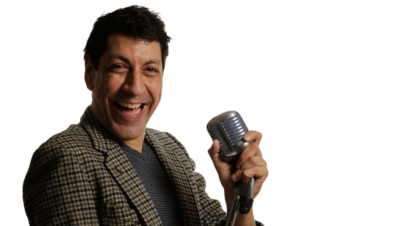 Indischer Stand-up-Künstler Rajnessh Kapoor steht am Mikrofon und lacht.