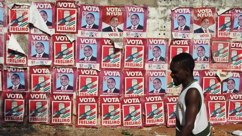 Ein Mann läuft in Maputo an einer Wand entlang, die mit roten Plakaten des mosambikanischen Staatschefs Filipe Jacinto Nyusi von der Frelimo beklebt ist.