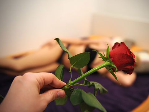 Eine Hand hält eine rote Rose vor eine Frau in Unterwäsche