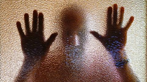 Ein Mann hinter einer nicht ganz transparenten Scheibe - die Hände am Glas