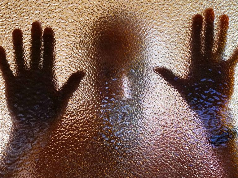 Ein Mann hinter einer nicht ganz transparenten Scheibe - die Hände am Glas