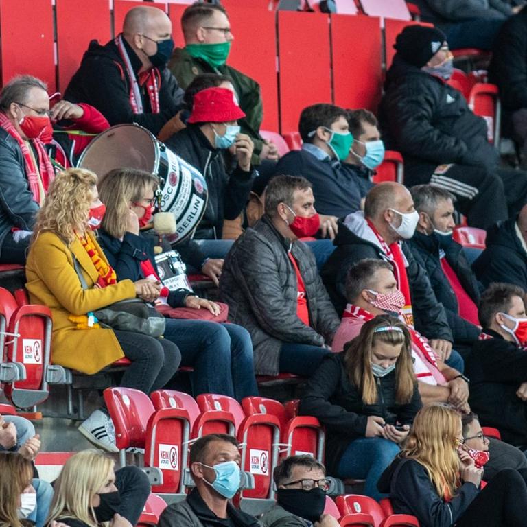 Fans von Union Berlin verfolgen das Spiel mit Abstand und Gesichtsmasken.