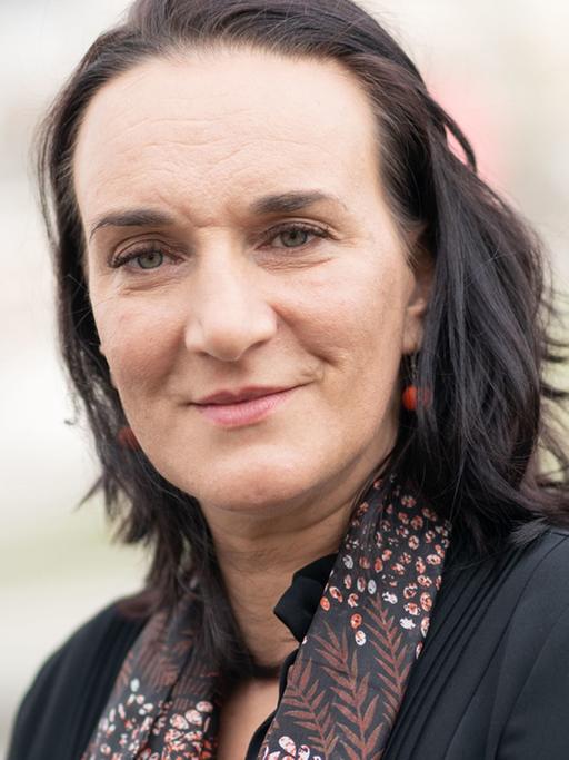 Porträt einer Frau mit schwarzen glatten Haaren, die direkt in die Kamera blickt.