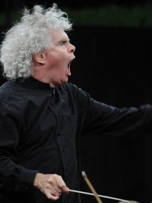 Dirigent Sir Simon Rattle bei einem Klassikkonzert in der Waldbühne, wobei sein Körper im Einsatz ist. Er dirigiert mit erhobenem Taktstock, geöffnetem Mund und Einsatz gebender linker Hand