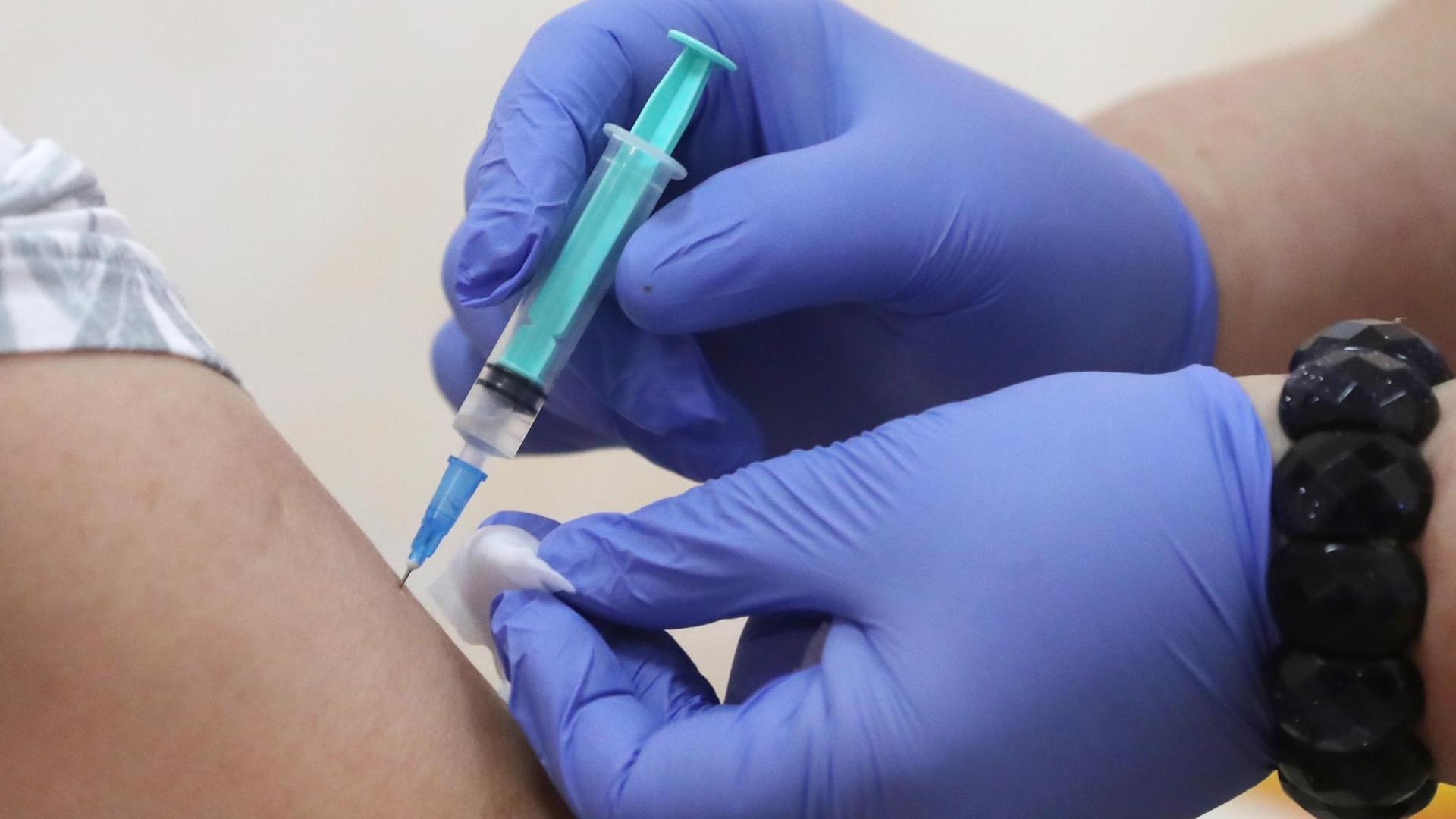 Impfung: Hände in blauen Schutzhandschuhen halten eine Spritze und einen Tupfer