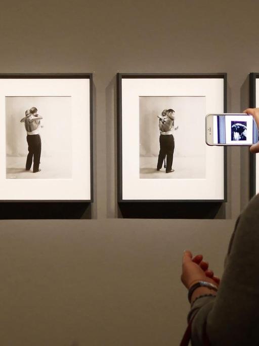 Eine Frau steht in einem Museum vor einem Bild und hält ein Handy davor.