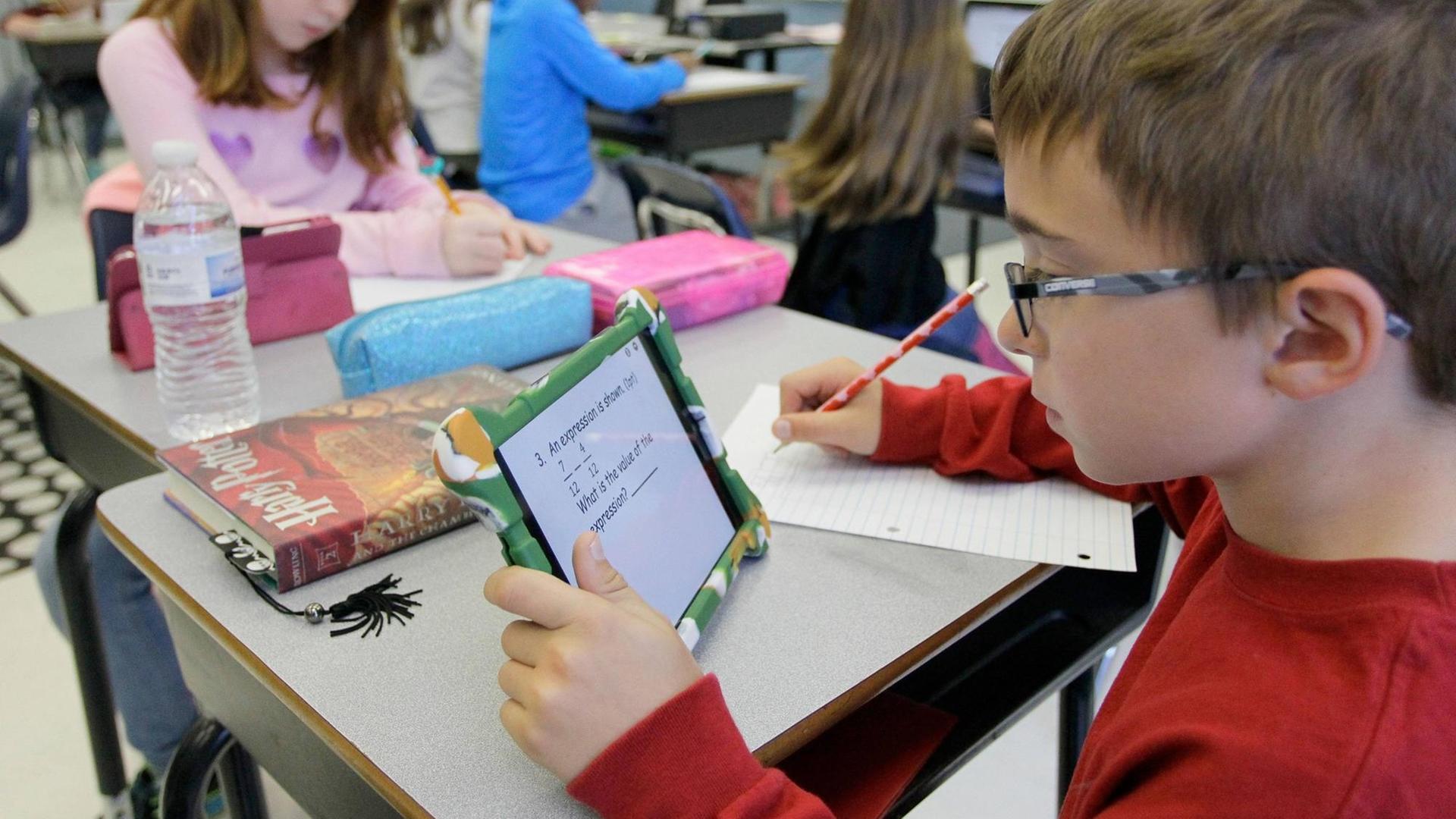 Ein Junge sitzt in einem Klassenraum und arbeitet mit einem Tablet.