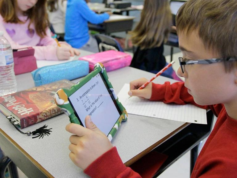 Ein Junge sitzt in einem Klassenraum und arbeitet mit einem Tablet.