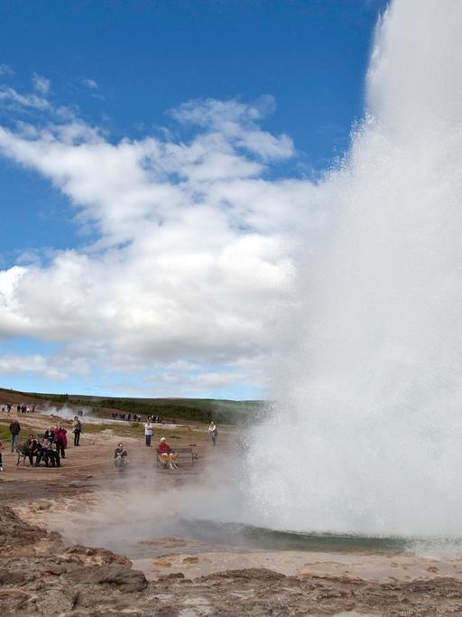 Touristen bestaunen den Geysir Strokkur auf Island.