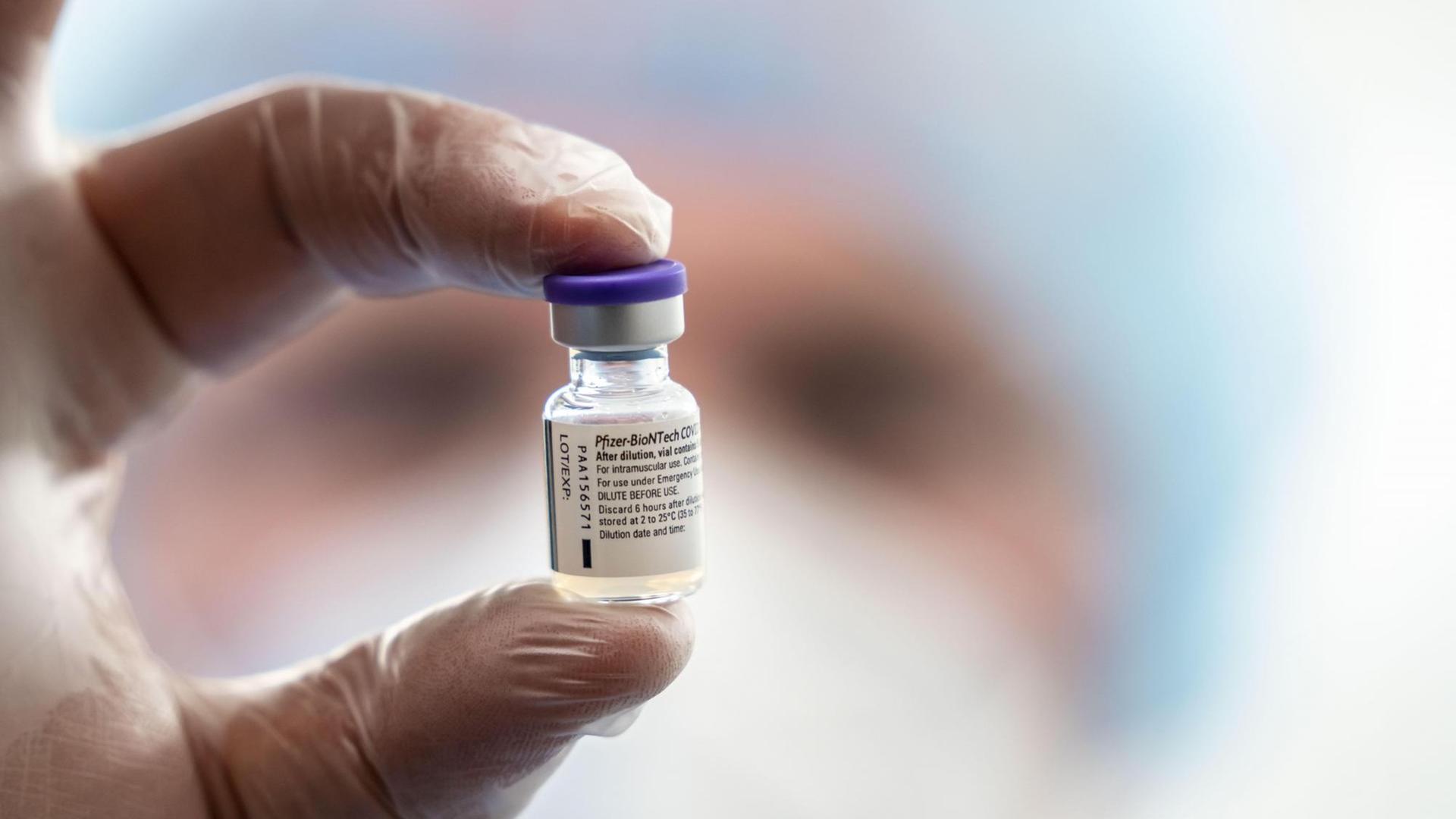 Zwei behandschuhte Finger halten eine kleine Ampulle mit dem Impfstoff von Biontech/Pfizer in der Luft