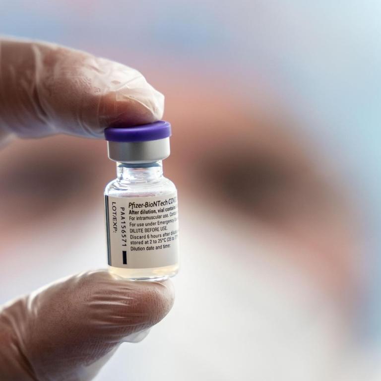 Zwei behandschuhte Finger halten eine kleine Ampulle mit dem Impfstoff von Biontech/Pfizer in der Luft