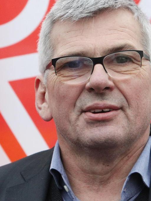IG-Metall-Chef Jörg Hofmann vor einer herunterhängenden Gewerkschaftsfahne.