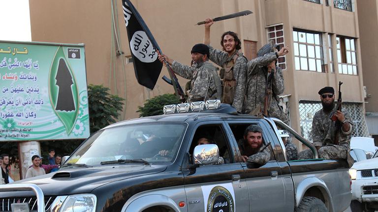 Angebliche Kämpfer der Terrorgruppe IS in der syrischen Stadt ar-Raqqa sitzen bewaffnet in und auf einem Auto.