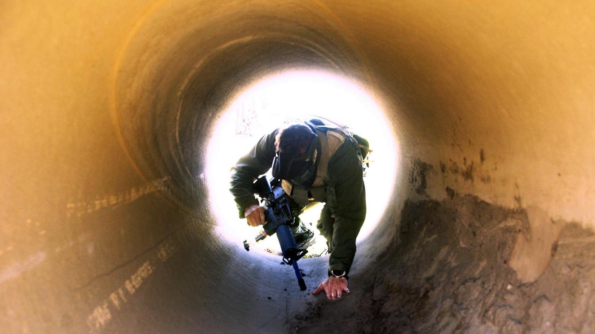 Mann in Soldatenkleidung mit Gewehr kriecht durch Tunnel