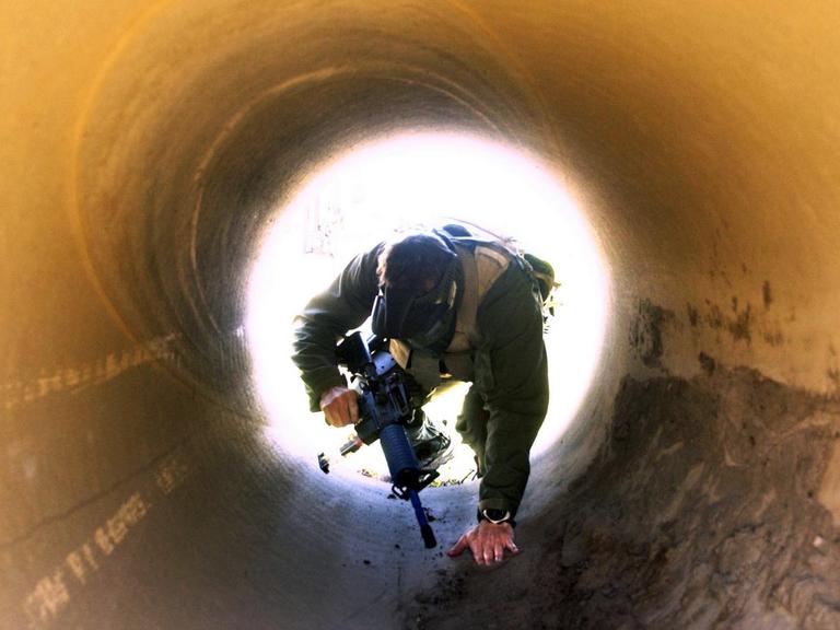 Mann in Soldatenkleidung mit Gewehr kriecht durch Tunnel