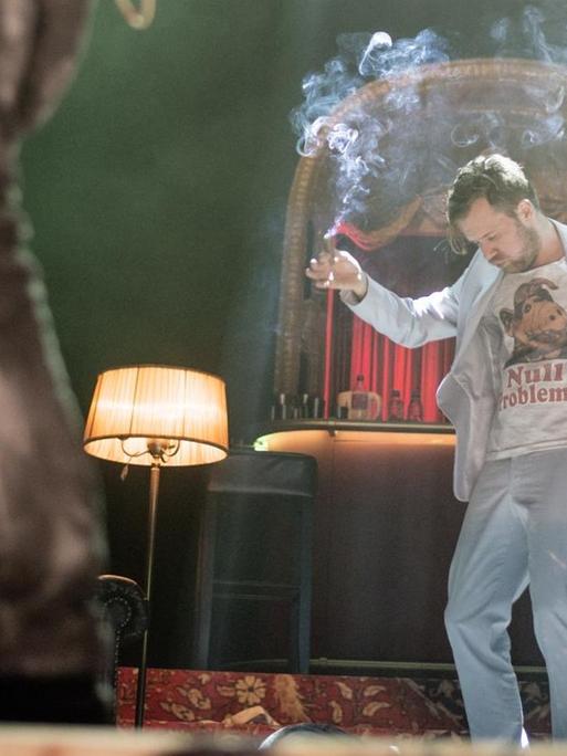 Der Schauspieler Nico Holonics hat in der einen Hand einen Bierbecher, in der anderen einen rauchenden Joint, Auf seinem T-Shirt steht "Null Probleomo".
