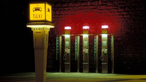 Eine Taxirufsäule und drei Telefonzellen bei Nacht.