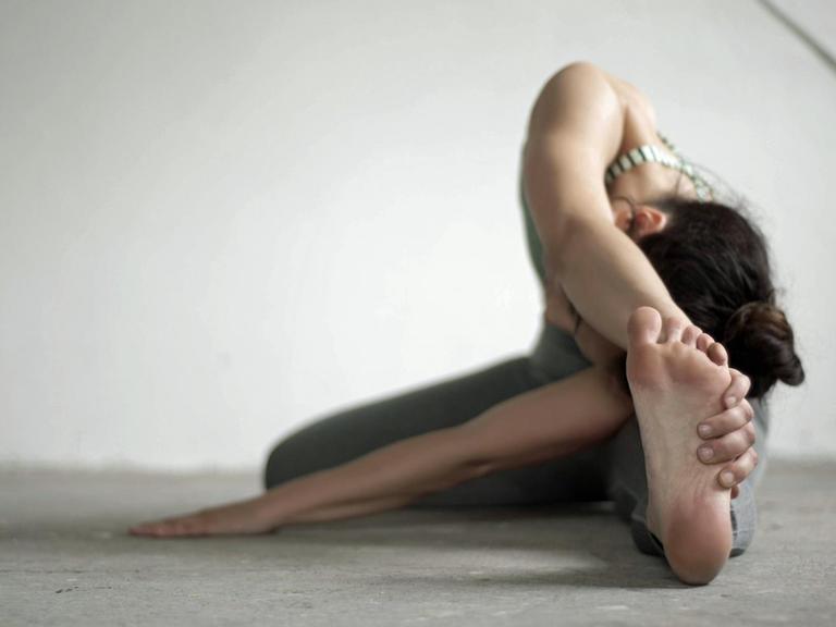 Eine Frau macht die Kopf-zum-Knie-Stellung im Yoga