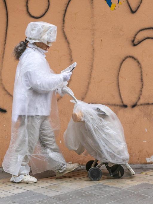 Eine in Plastikfolie gehüllte Frau geht an einer Mülltonne vorbei.