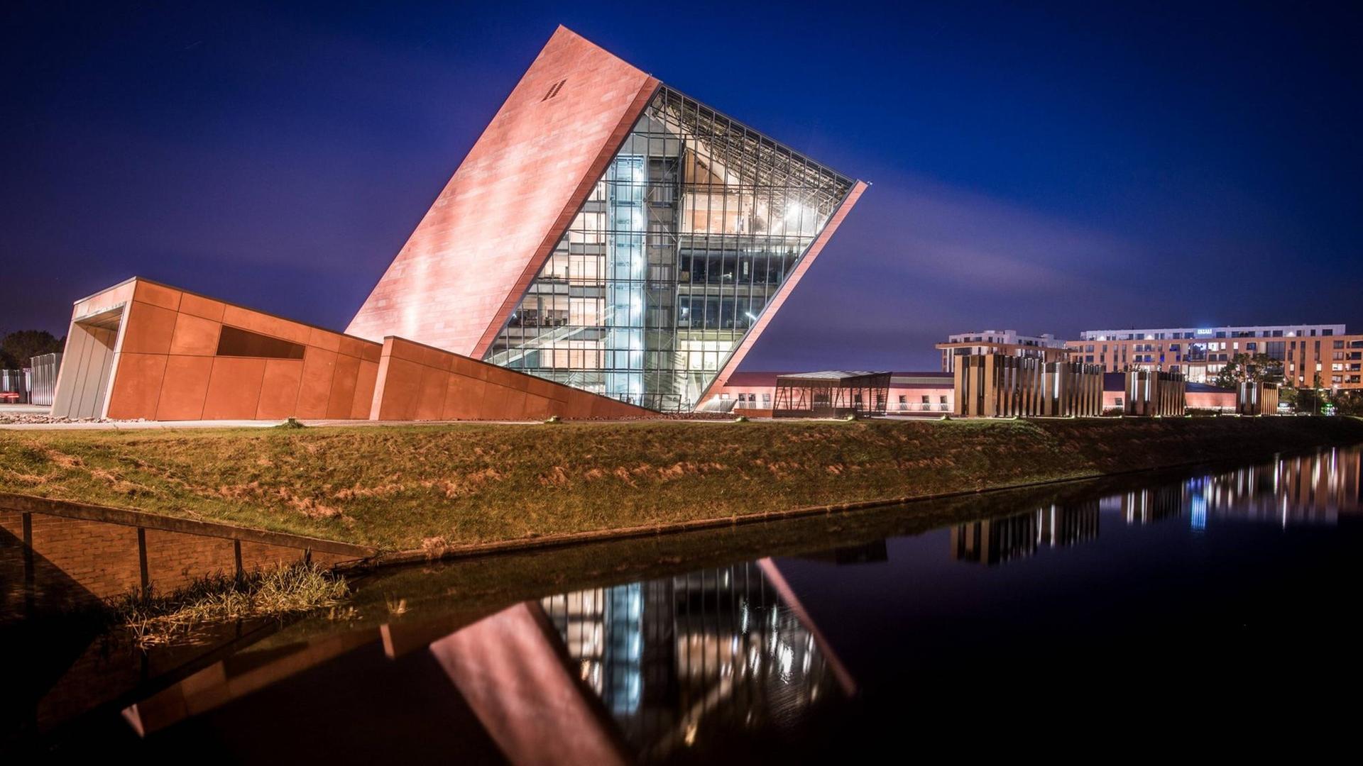 Der Museumsbau des Architekturbüro Kwadrat in Gdynia in Form eines schräg aus dem Boden ragenden und teilweise verglasten Würfels in nächtlicher Beleuchtung.