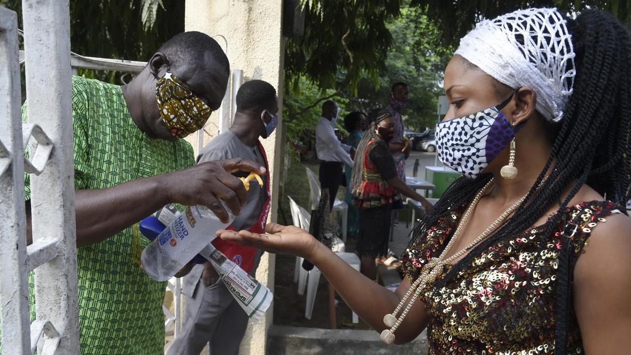 Eine schwarze Frau mit Maske desinfiziert sich in Nigeria vor dem Kirchenbesuch die Hände.