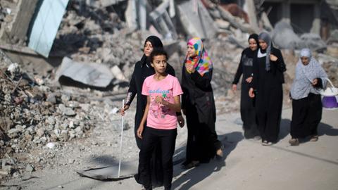 Palästinensische Zivilisten laufen während einer brüchigen Waffenruhe am 01.08.2014 an einem Berg von Schutt vorbei.