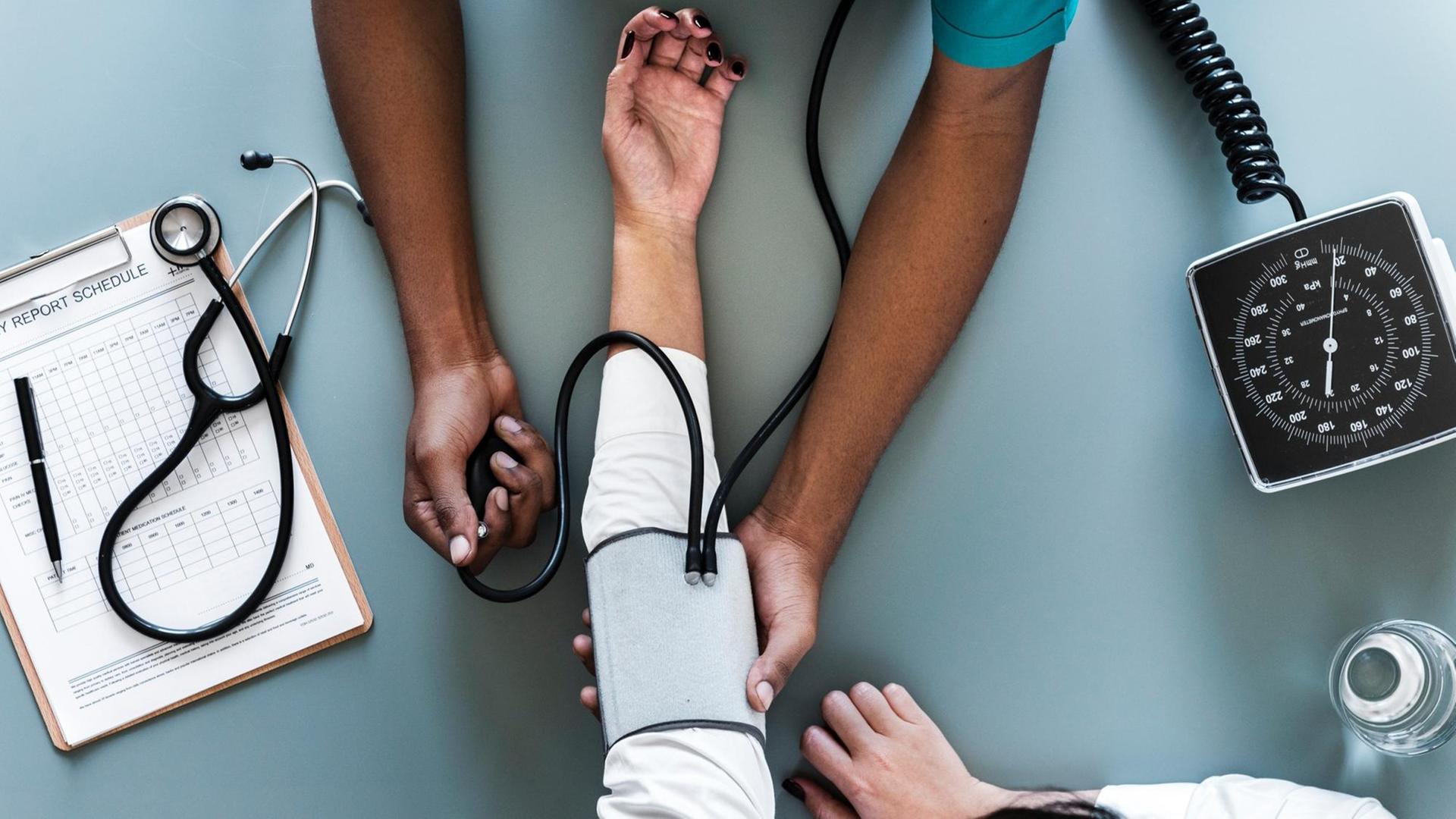 An einem Unterarm wird der Puls gemessen, drumherum liegt weiteres medizinisches Equipment