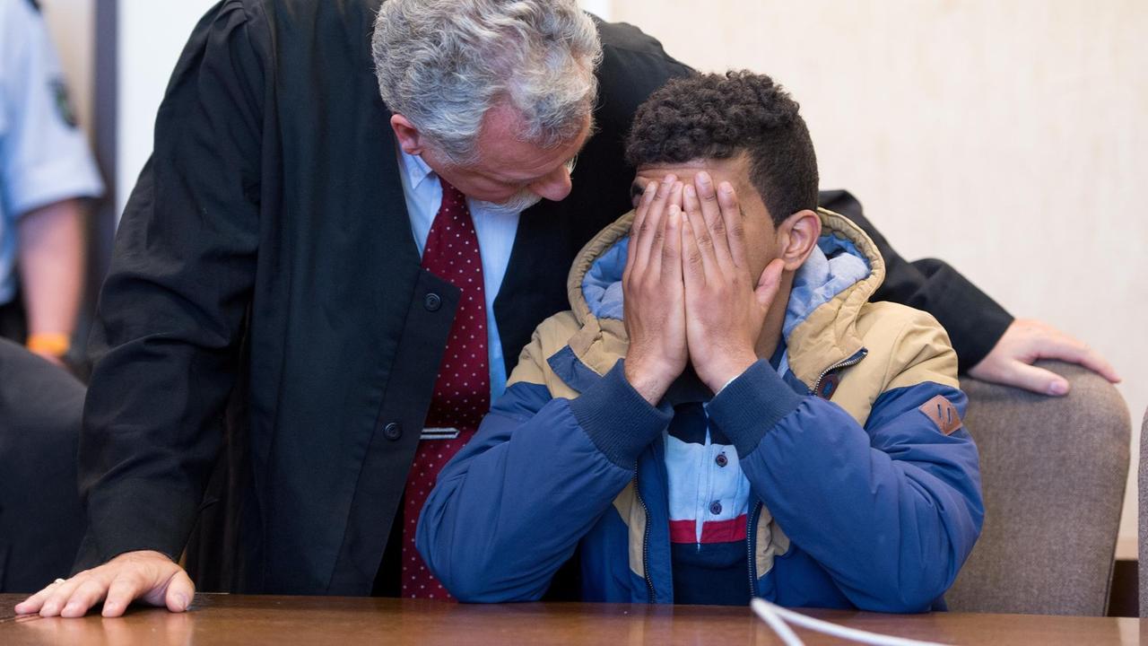 Der 23-jährige angeklagte Algerier hält sich die Hände vors Gesicht. Sein Anwalt steht neben ihm im Gerichtssaal des Amtsgerichts in Köln am 6.5.2015.